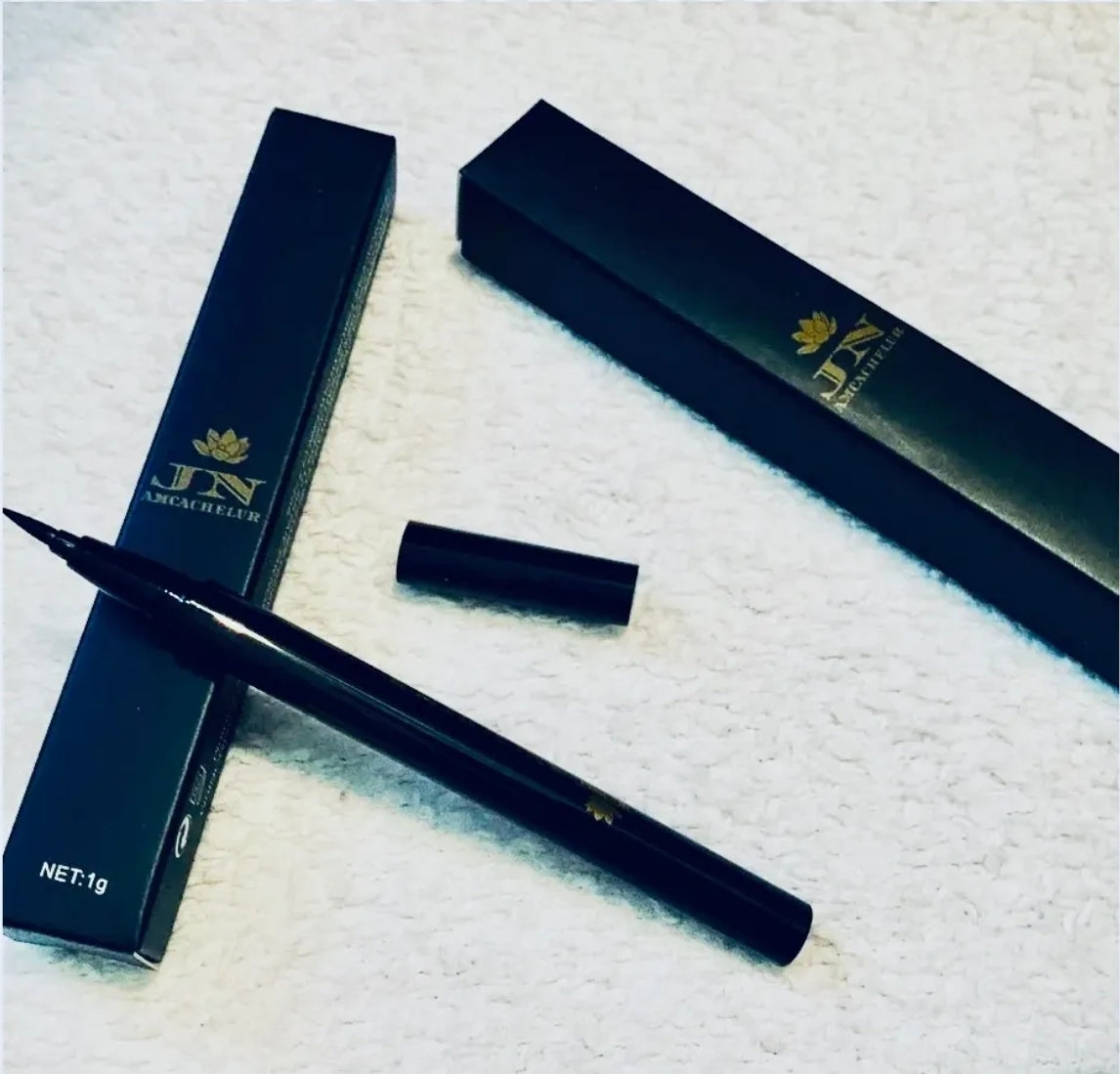 Black JNA eyeliner liquid pen resting on its box.